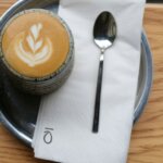 Close-up of latte art in ceramic cup on metal tray with Kohi coffee branding napkin
