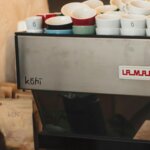 Close-up of espresso machine with Kohi logo and stacked branded coffee cups