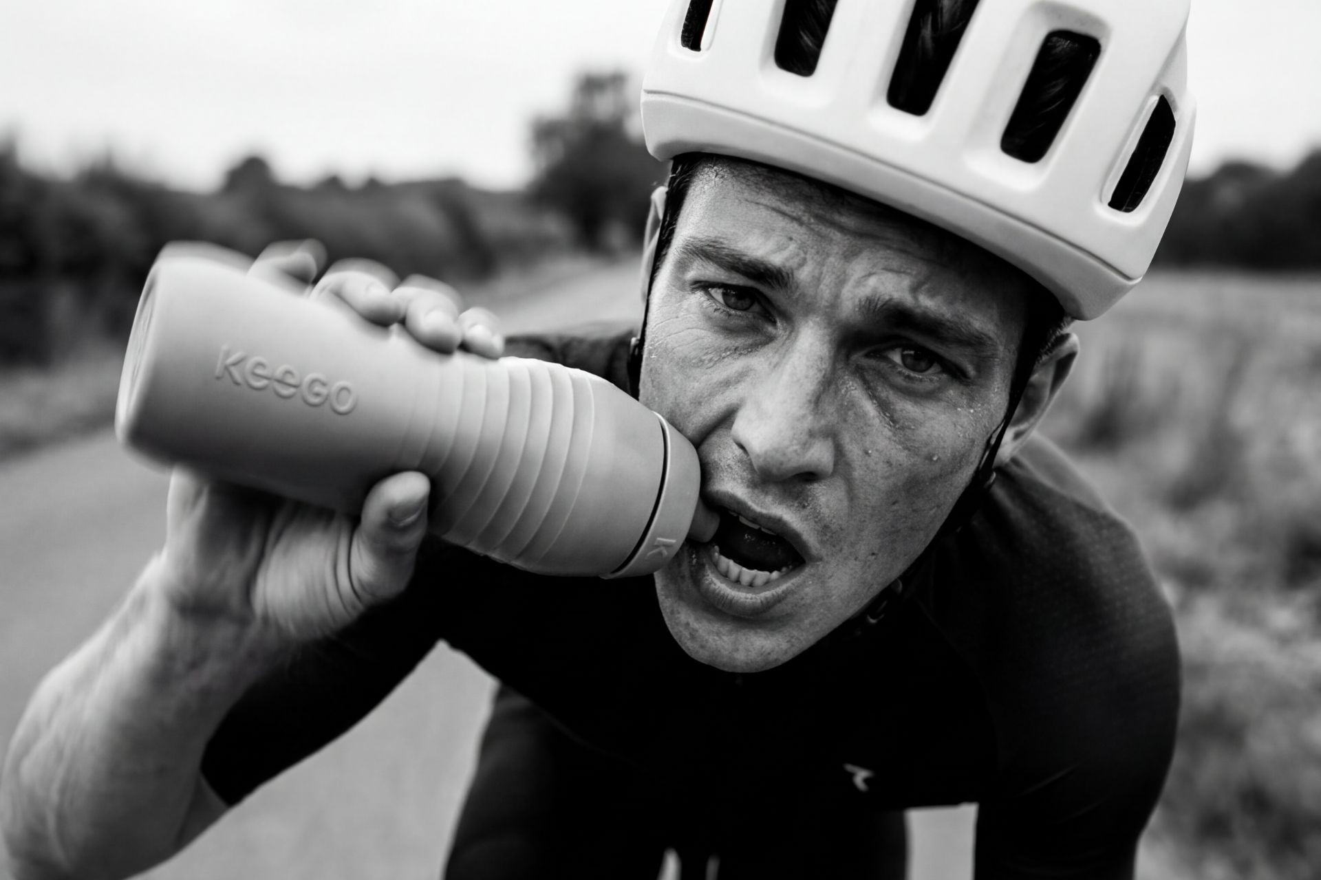 Male cyclist drinking from bottle during ride, close-up portrait on rural road, outdoor cycling scene