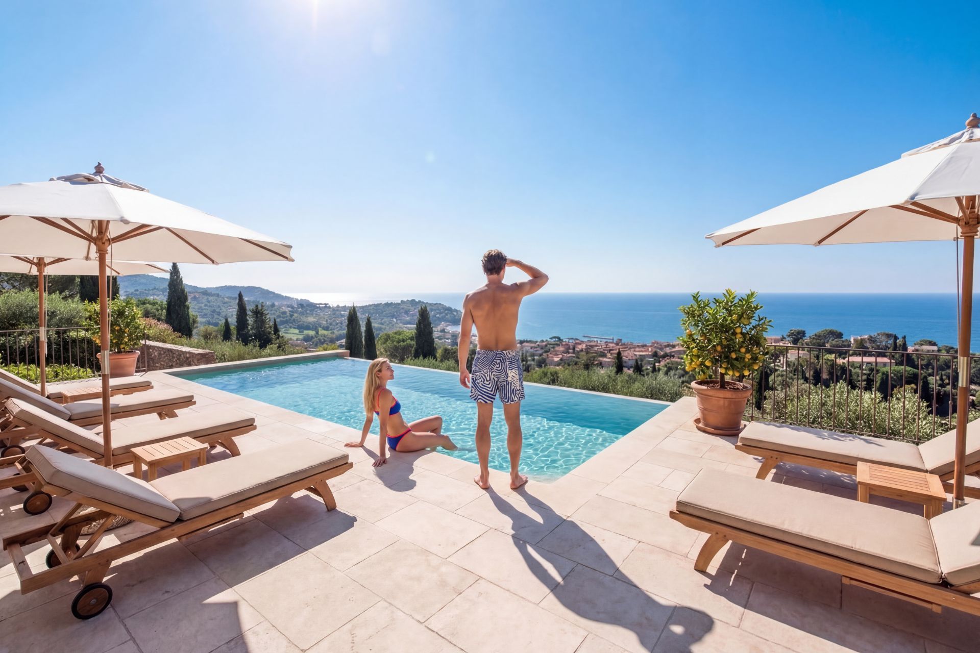 woman sitting at pool edge and man standing, overlooking sea and coastal town